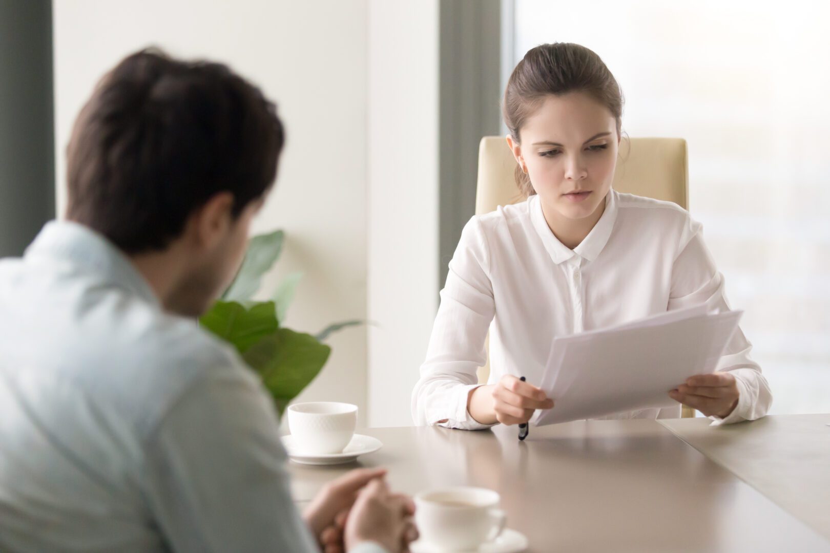 Serious businesswoman studying papers sitting opposite man at of Concentrated female boss attentively studying agreement or contract before signing during meeting with partner. Businesswoman reading finance report, hr manager looking through resume of candidate